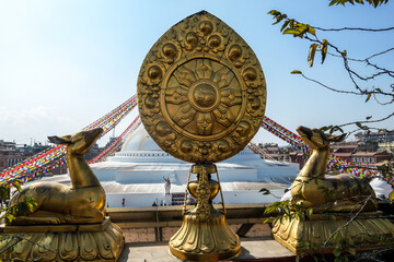 Two golden deers sitting around a golden monument with the view on Boudhanath Temple in Kathmandu, Nepal. Prayer flags attached to the temple. Spirituality and meditation