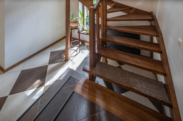 Close-up of wooden staircase to the second floor in private house. Luxury interior of apartment. Green plant near window.