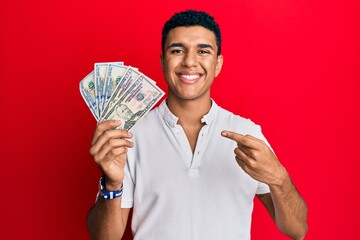 Young arab man holding dollars smiling happy pointing with hand and finger