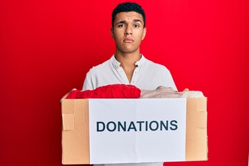 Young arab man holding donation box with clothes skeptic and nervous, frowning upset because of...