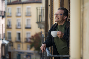 lifestyle portrait of happy and cheerful mature man 65 to 70 years old at home balcony feeling positive and relaxed drinking coffee enjoying retirement smiling to the street view