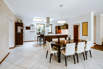 Modern interior of spacious luxury studio apartment. Wooden table and chairs. Kitchen set. White walls and tile floor.