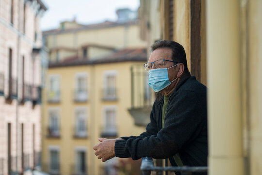 mature man in balcony home lockdown during covid19 outbreak - senior male on his 70s in face mask worried and tired looking to the street thoughtful and depressed in quarantine