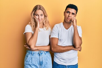 Young interracial couple wearing casual white tshirt thinking looking tired and bored with depression problems with crossed arms.