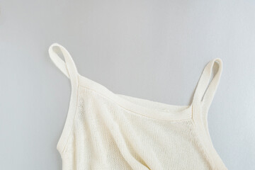Top of soft crumpled white knitted sleeveless female shirt lying on light grey background close...