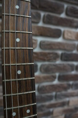 Close-up of a guitar neck. Brick background.