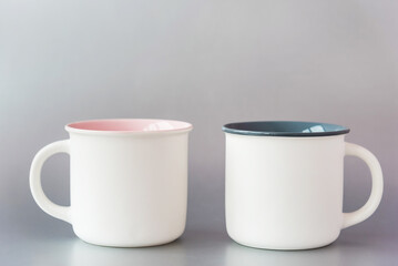 Elegant white cups with pink and green color inside and mockup for design on sides standing on light grey background extreme close view. Contemporary dishware.