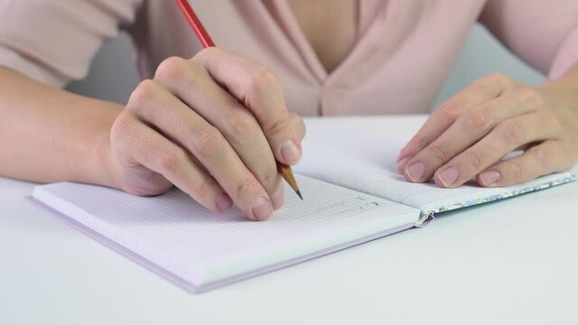 Woman holding red pencil and writing something in a notebook, goal setting and planning concept