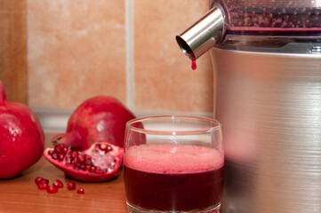Pressing the pomegranate juice with a juicer into a glass. Making juice at home.