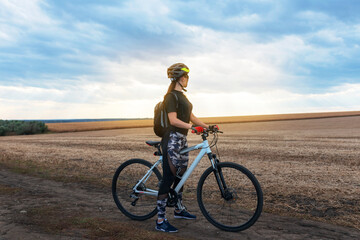 Fototapeta premium girl standing with a bicycle in the middle of the evening field