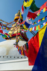 The Bouddhanath Temple in Kathmandu, Nepal. The temple has many colourful prayer flags with 'om mani padme hum' mantra written on them attached to it's golden rooftop. Spirituality and meditation.