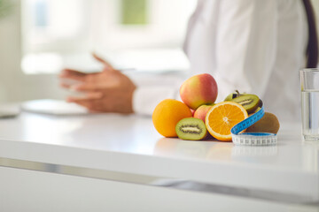 Appetizing fruit and measuring tape on desk against blurred dietitian giving weight loss advice