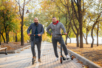 Young guys ride in the Park on an electric scooter on a warm autumn day. Walk in the Park.