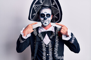 Young man wearing mexican day of the dead costume over white smiling cheerful showing and pointing with fingers teeth and mouth. dental health concept.