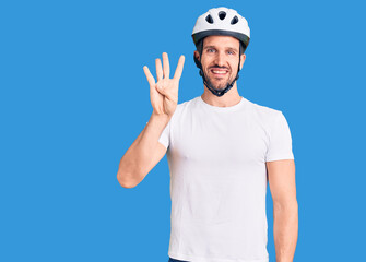 Young handsome man wearing bike helmet showing and pointing up with fingers number four while smiling confident and happy.