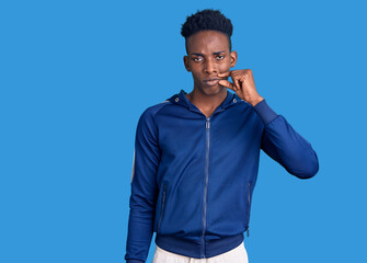 Young african american man wearing sportswear mouth and lips shut as zip with fingers. secret and...