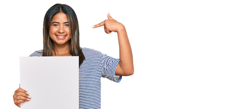Young latin girl holding blank empty banner pointing finger to one self smiling happy and proud