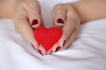 Red knitted heart in female hands on a bed. Concept of love, Valentines day celebration, motherhood, blood donation