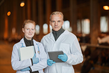 Fototapeta na wymiar Waist up portrait of two smiling veterinarians at farm looking at camera while holding tablets, copy space