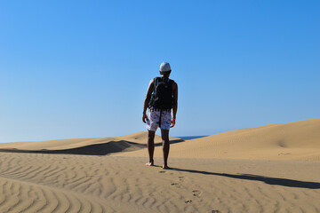 Lonely traveler walking through desert sand dunes with backpack.