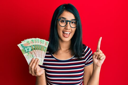 Beautiful asian young woman holding 50 hong kong dollars banknotes smiling with an idea or question pointing finger with happy face, number one