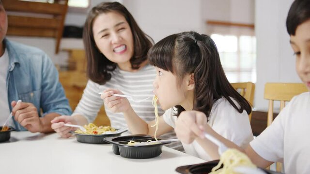 Happy cheerful Asian family having lunch eat spaghetti pasta in plastic container in dining room at modern home. Spending time together, Self-isolation, Social distancing, Quarantine for corona virus.