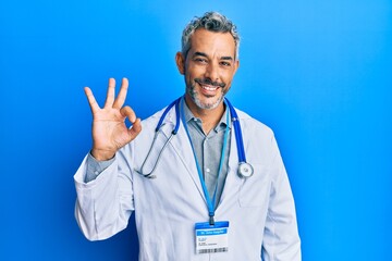 Middle age grey-haired man wearing doctor uniform and stethoscope smiling positive doing ok sign with hand and fingers. successful expression.