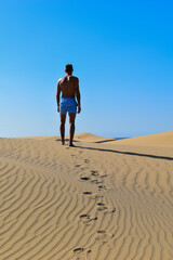 Fototapeta na wymiar Man walking in a swimming trunks through the desert under the sun.