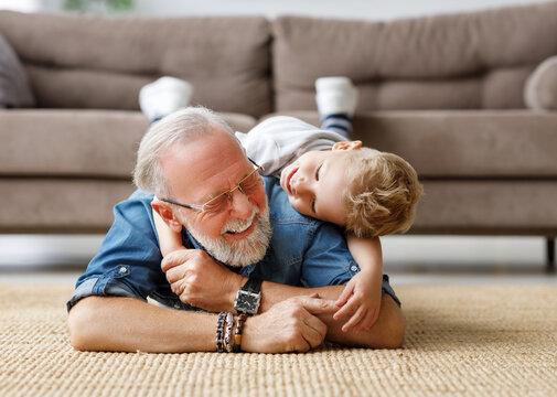 Cheerful kid boy hugging grandfather at home.