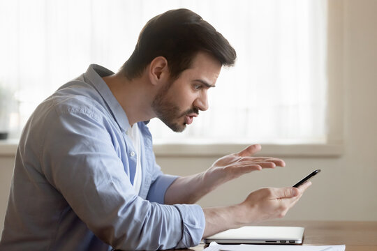 But How... Angry Mad Shocked Millennial Male Brawling By Mobile Phone With Client Support Of Bank Online Shop Store Scolding Bad Service Poor Quality Of Goods Purchased Slow Incorrect Application Work