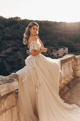beautiful bride with blond hair in luxurious wedding dress posing in balcony with beautiful view of...