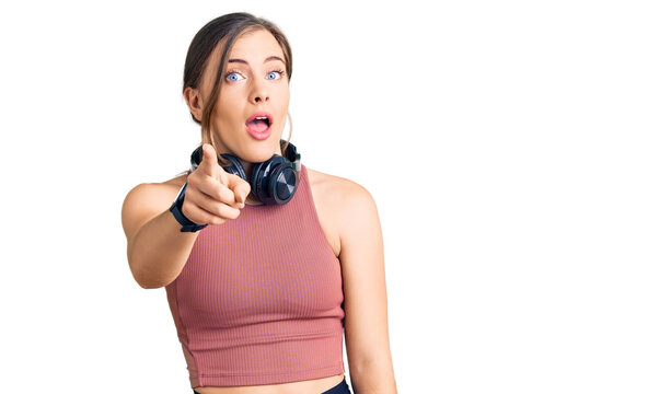 Beautiful caucasian young woman wearing gym clothes and using headphones pointing displeased and frustrated to the camera, angry and furious with you