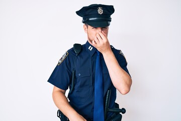 Young caucasian man wearing police uniform smelling something stinky and disgusting, intolerable...