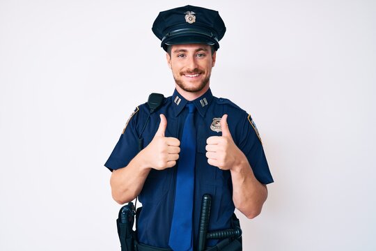 Young caucasian man wearing police uniform success sign doing positive gesture with hand, thumbs up smiling and happy. cheerful expression and winner gesture.