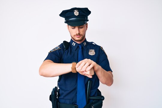 Young caucasian man wearing police uniform checking the time on wrist watch, relaxed and confident