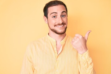 Young handsome man wearing casual clothes smiling with happy face looking and pointing to the side with thumb up.