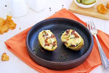 Twice baked potatoes with cheese and chanterelle mushrooms on a brown clay plate on a light concrete background. Recipes with potatoes.