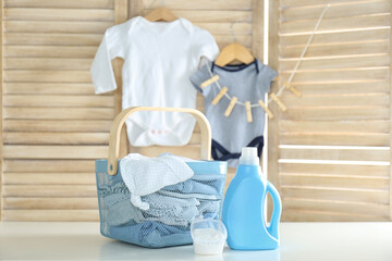 Basket with baby laundry, bottle of detergent and washing powder on white table