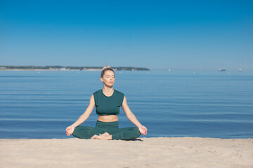 Fototapeta na wymiar Woman in green sportswear practices yoga by sea