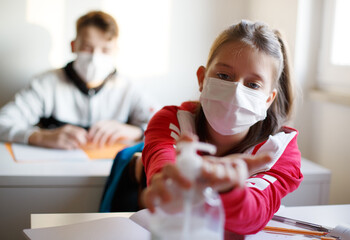 School girl with face mask at school disinfecting hands.