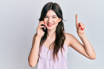 Young beautiful caucasian girl having conversation talking on the smartphone smiling with an idea or question pointing finger with happy face, number one