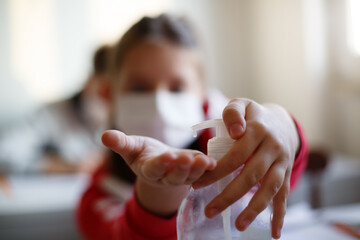 School girl with face mask at school disinfecting hands.