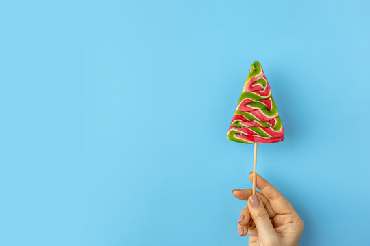 Woman hand hold tasty candies on on blue background. Candy shapes, candy cane. Flat lay, top view. Copy space