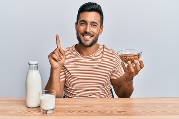 Handsome hispanic man drinking healthy almond milk smiling with an idea or question pointing finger with happy face, number one