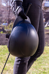 Woman in black gloves holding horse back riding helmet and whip in her hands. Equestrian equipment