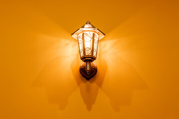 the lantern shines casting a shadow on the yellow wall