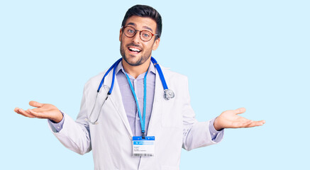 Young hispanic man wearing doctor uniform and stethoscope smiling showing both hands open palms, presenting and advertising comparison and balance