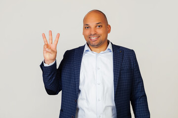 Portrait of a successful young African American businessman guy, showing with fingers to number three, smiling, confident and happy. The man shows three fingers. Number 3.  gray background.