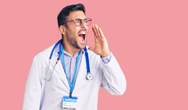 Young hispanic man wearing doctor uniform and stethoscope shouting and screaming loud to side with hand on mouth. communication concept.