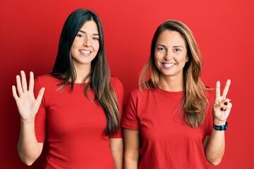 Hispanic family of mother and daughter wearing casual clothes over red background showing and...
